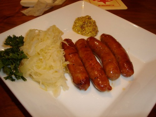 A plate with four grilled sausages, sauerkraut, mustard, and a sprig of parsley.
