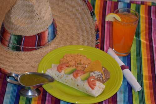 A colorful plate of Mexican food with a sombrero, a drink, and a vibrant striped tablecloth.