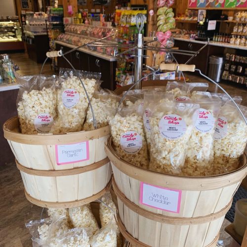Two wooden baskets filled with bags of popcorn, labeled Parmesan Garlic and White Cheddar, in a colorful store.