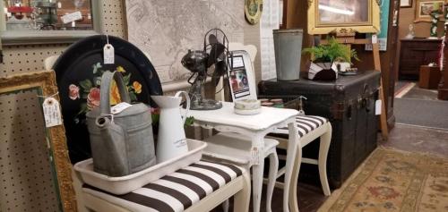 A vintage display featuring chairs, a small table, decorative items, and an antique trunk in a cozy shop setting.