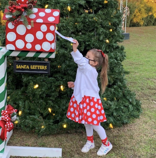 A girl in a polka dot skirt places a letter in a festive mailbox decorated for Christmas.