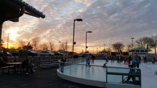 A sunset over an outdoor ice skating rink with people skating and enjoying the evening.