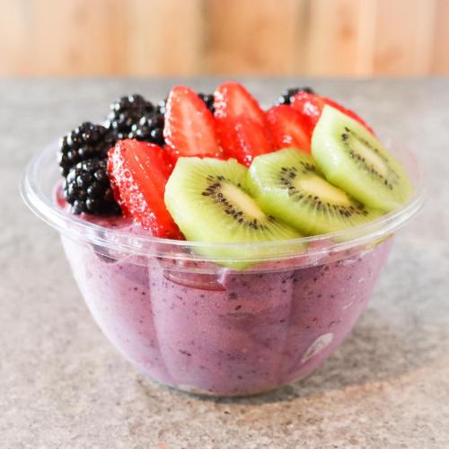 A clear bowl filled with purple smoothie topped with sliced strawberries, kiwi, and blackberries.