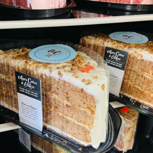 Two packaged carrot cakes with cream cheese frosting and nuts, displayed on a shelf at a bakery.
