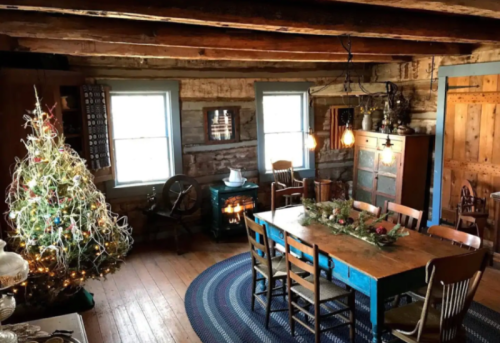 Cozy rustic dining room with a decorated Christmas tree, wooden furniture, and warm lighting.