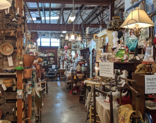 A cozy antique shop filled with various vintage items, lamps, and decor, with signs indicating a sale.