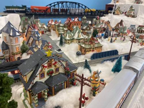 A festive miniature village with colorful houses, snow, and a train track running through it, decorated for the holidays.