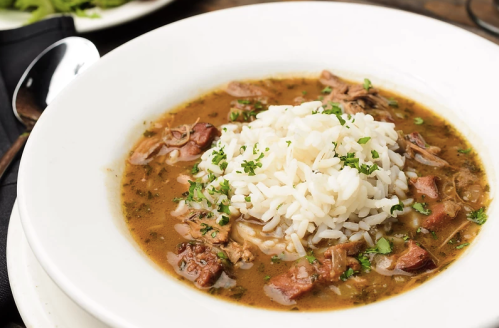 A bowl of hearty soup with shredded meat, herbs, and a mound of white rice on top, garnished with parsley.