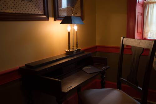 A vintage desk with a lamp, illuminated softly, beside a wooden chair in a warmly colored room.