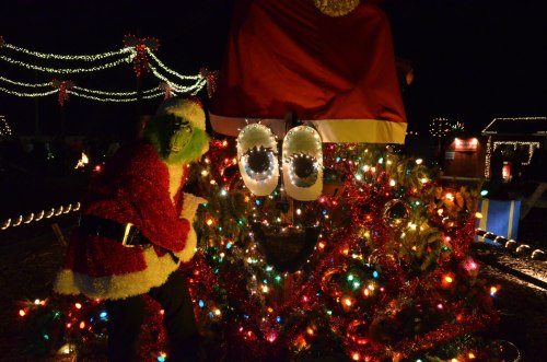 A festive scene featuring the Grinch in a Santa suit next to a decorated Christmas tree with colorful lights.