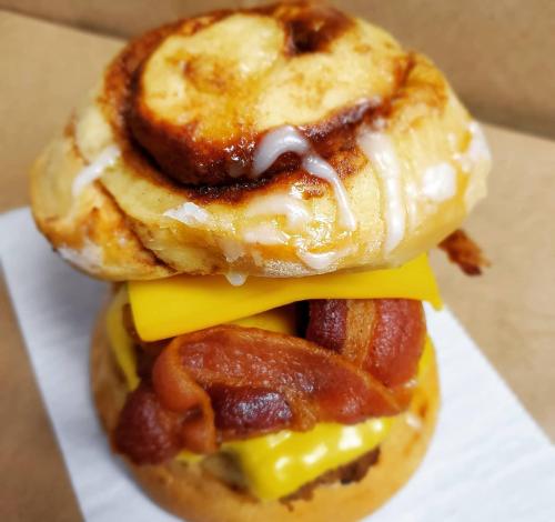 A decadent sandwich featuring a cinnamon roll top, bacon, cheddar cheese, and a savory sausage patty.