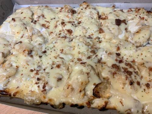A close-up of a cheesy pizza topped with crispy bacon bits, baked to a golden brown in a cardboard box.