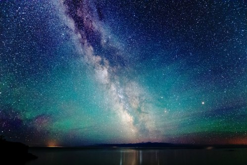 A stunning night sky filled with stars and the Milky Way, reflecting over a calm body of water.