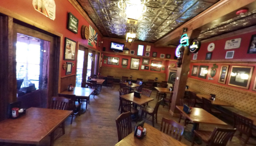 Cozy restaurant interior with wooden tables, chairs, and vintage decor, featuring a bar and a TV in the background.