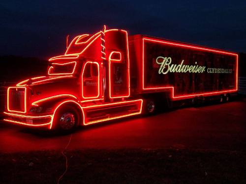 A brightly lit Budweiser truck with neon red lights against a dark background.