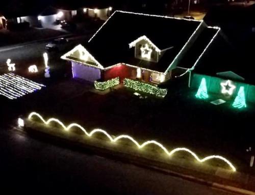 A house decorated with colorful Christmas lights, featuring stars, trees, and a lighted pathway in a festive display.