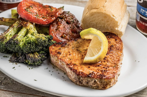 Grilled salmon with lemon, served with roasted broccoli, tomatoes, and a bread roll on a white plate.