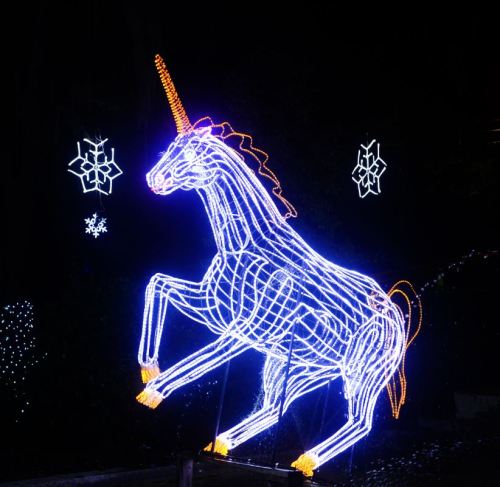 A glowing unicorn sculpture made of colorful lights, set against a dark background with decorative snowflakes.