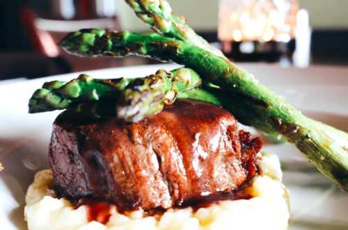 A gourmet dish featuring a tender beef filet on creamy mashed potatoes, topped with asparagus and a rich sauce.