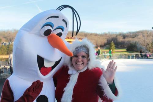 A person in a Santa costume poses with a large snowman character, both smiling on an outdoor ice rink.