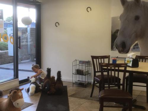 A child interacts with plush horses in a cozy indoor space, with a large horse mural on the wall.