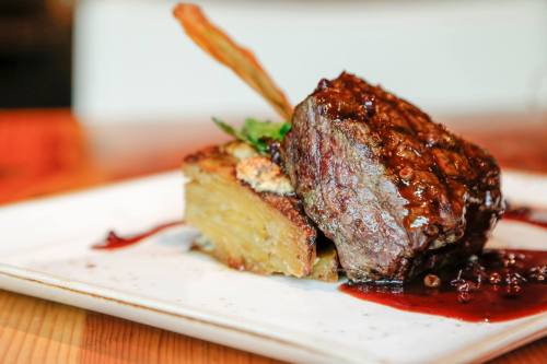 A plated dish featuring a juicy steak with a rich sauce, served on a bed of potatoes and garnished with herbs.
