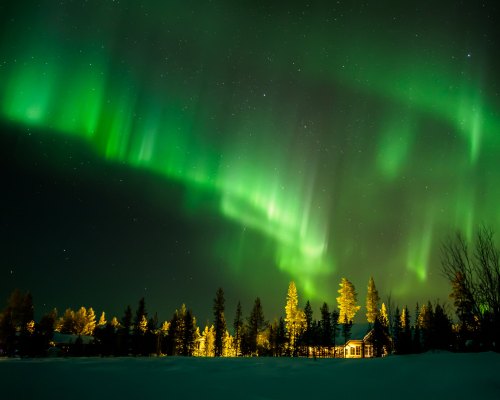 A stunning display of the Northern Lights illuminates the night sky above a snowy landscape and a cozy cabin.