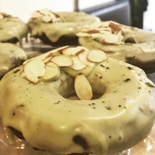 Close-up of green-glazed donuts topped with sliced almonds, resting on a clear display.