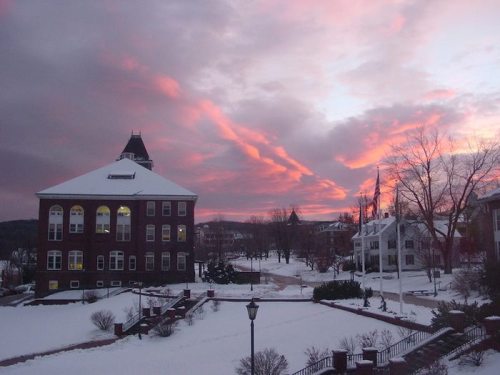 A snowy campus scene at sunset, with vibrant pink and purple clouds above a historic brick building.
