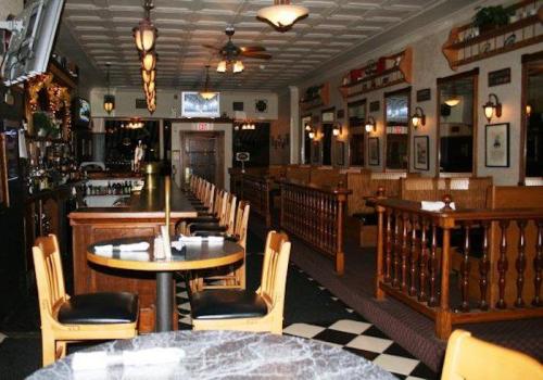 Interior of a cozy restaurant featuring wooden furniture, a bar area, and checkered flooring.