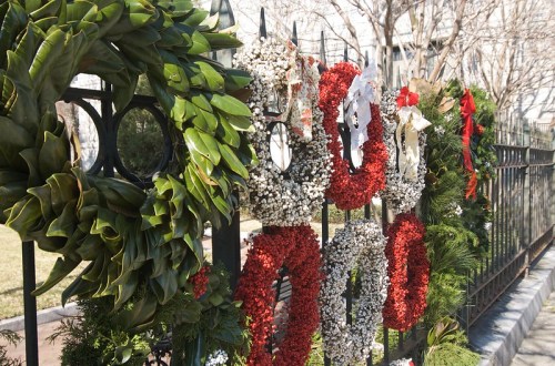 A variety of festive wreaths in red, white, and green hanging on a decorative fence.
