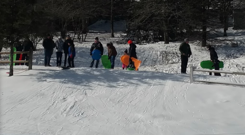 A group of people standing in the snow, holding colorful sleds, preparing to go down a hill.