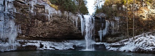 A frozen waterfall cascades over rocky cliffs, surrounded by icicles and a serene, icy landscape.