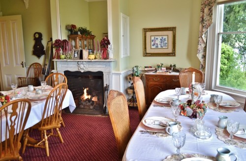 A cozy dining room with a fireplace, elegantly set tables, and floral decor, creating a warm, inviting atmosphere.