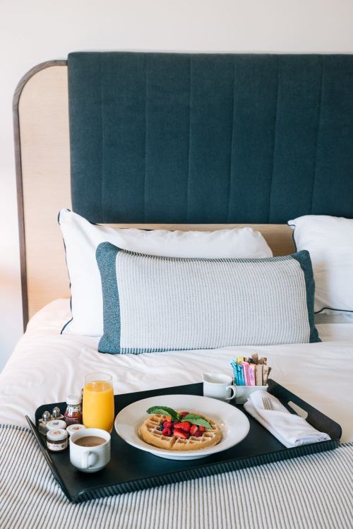 A cozy hotel bed with a breakfast tray featuring waffles, fruit, orange juice, and coffee.