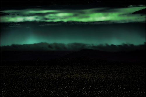A dark landscape with a greenish glow in the sky, featuring clouds and distant mountains under a night sky.