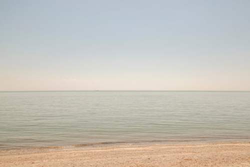 A calm, serene beach scene with gentle waves lapping at the shore under a clear sky.