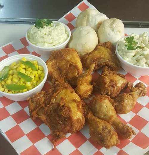 A platter of fried chicken, rolls, corn, and two bowls of creamy sides on a checkered paper.