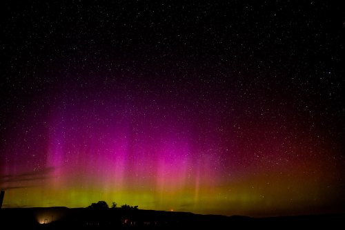 A vibrant aurora borealis lights up the night sky with shades of purple and green against a backdrop of stars.