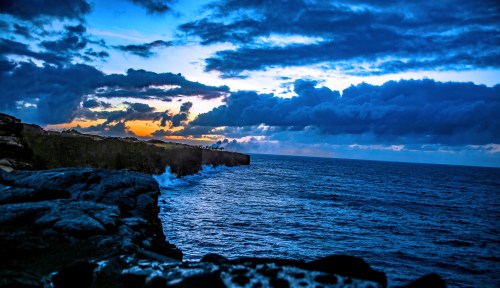 A dramatic coastline at sunset, with dark clouds and vibrant colors reflecting on the ocean waves.