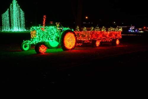 A brightly lit green tractor with a red trailer, decorated with colorful lights against a dark night sky.