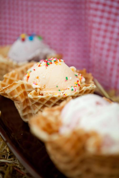 Three scoops of ice cream in waffle cones, topped with colorful sprinkles, arranged on a plate.