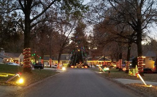 A festive neighborhood street decorated with colorful Christmas lights and trees, creating a joyful holiday atmosphere.