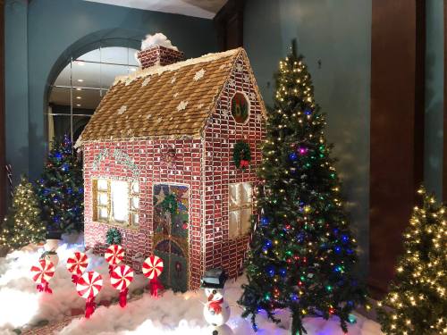 A festive gingerbread house surrounded by colorful Christmas trees and candy canes, with snow-like decorations.