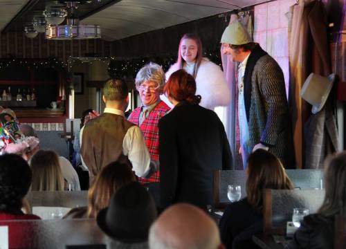 A lively performance on a train with actors in costumes entertaining an audience seated at tables.