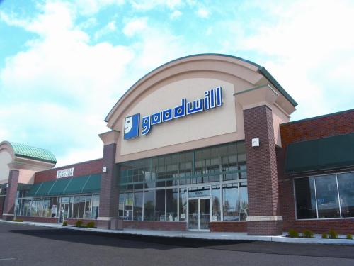 Exterior of a Goodwill store with a large sign, featuring a brick facade and green awnings under a cloudy sky.