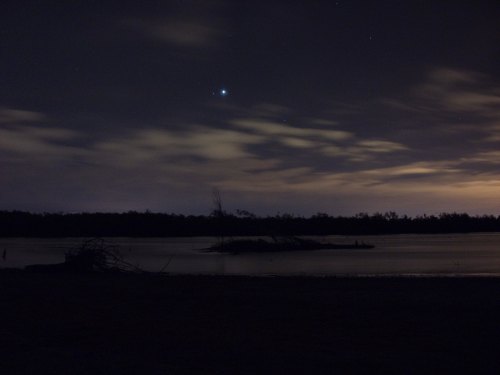 A serene night scene of a calm river with clouds and stars, reflecting soft light from the horizon.