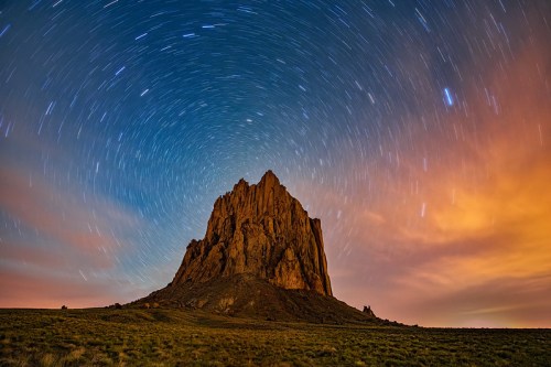 A dramatic rock formation under a starry sky, with swirling stars and a colorful twilight backdrop.