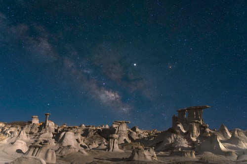 A starry night sky over unique rock formations, with the Milky Way visible in the background.