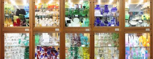 A display of colorful glassware and crystal pieces in wooden cabinets, showcasing various shapes and sizes.